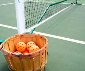 A basket of orange balls on a tennis court.