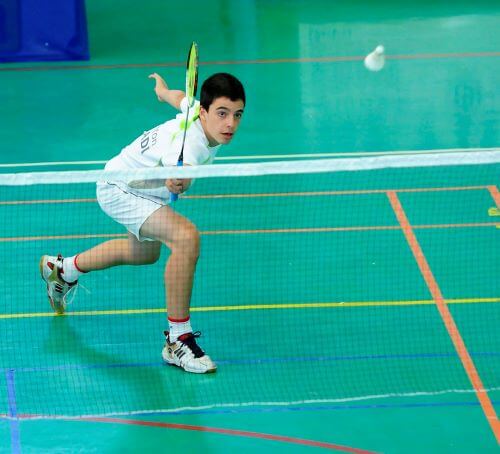 A young boy playing badminton on a court.