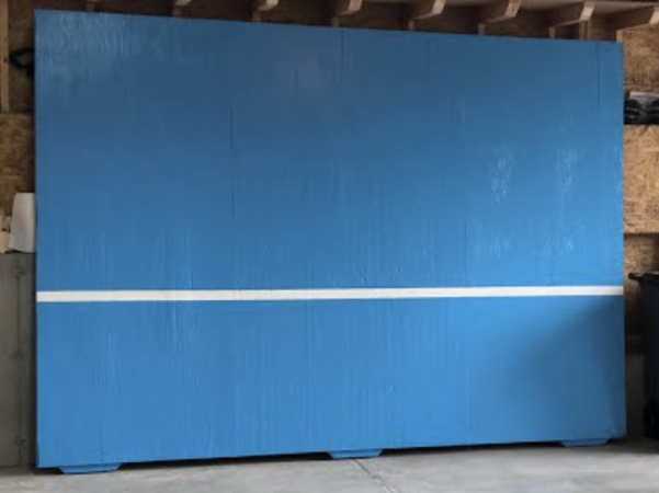 Homemade blue pickleball practice wall with white painted net line.
